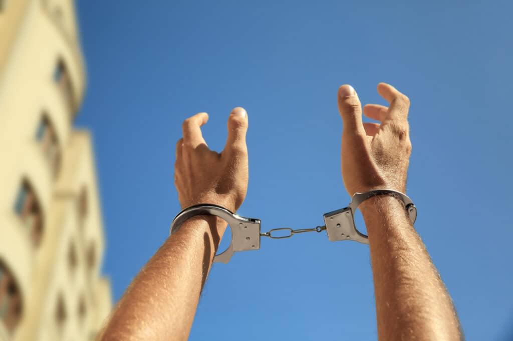 Man in handcuffs against blue sky outdoors, closeup